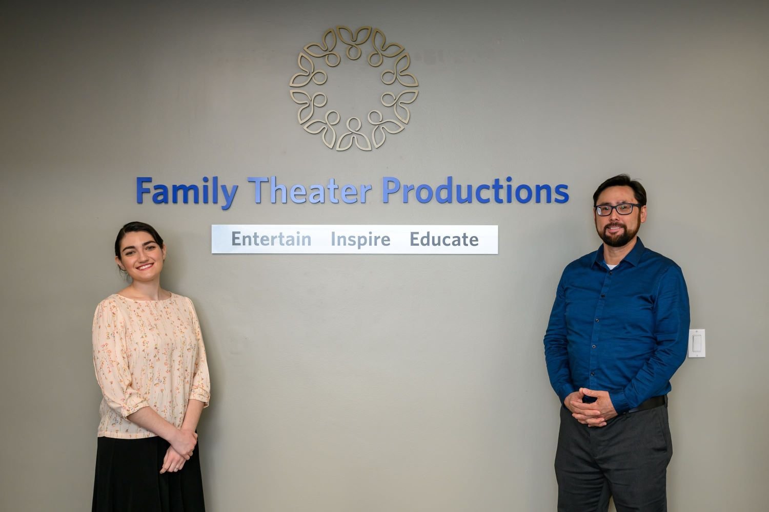 two family theater production staff members standing in front of the logo in the lobby